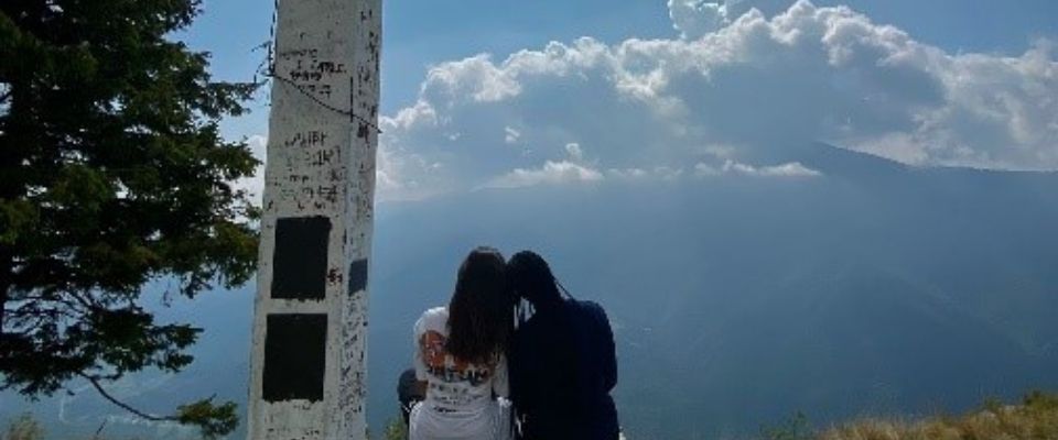 2 lány ül háttal egy dombtetőn egy villanyoszlop mellett fejüket egymásnak hajtva Szemben velük az ég látszik felhőkkel