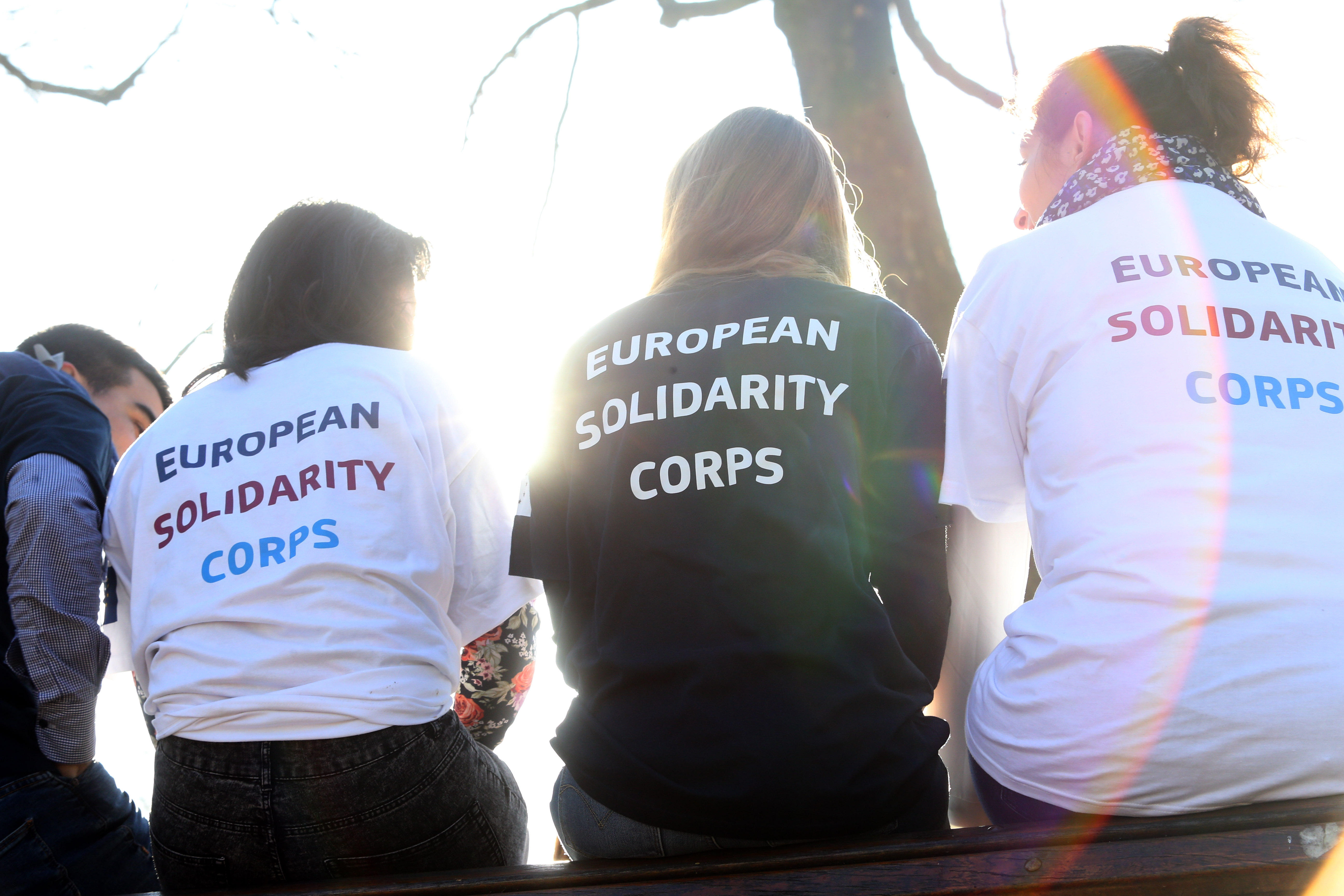 European Solidarity Corps feliratú pólóban a szabadban a kamerának háttal üldögélő 4 fiatal képe