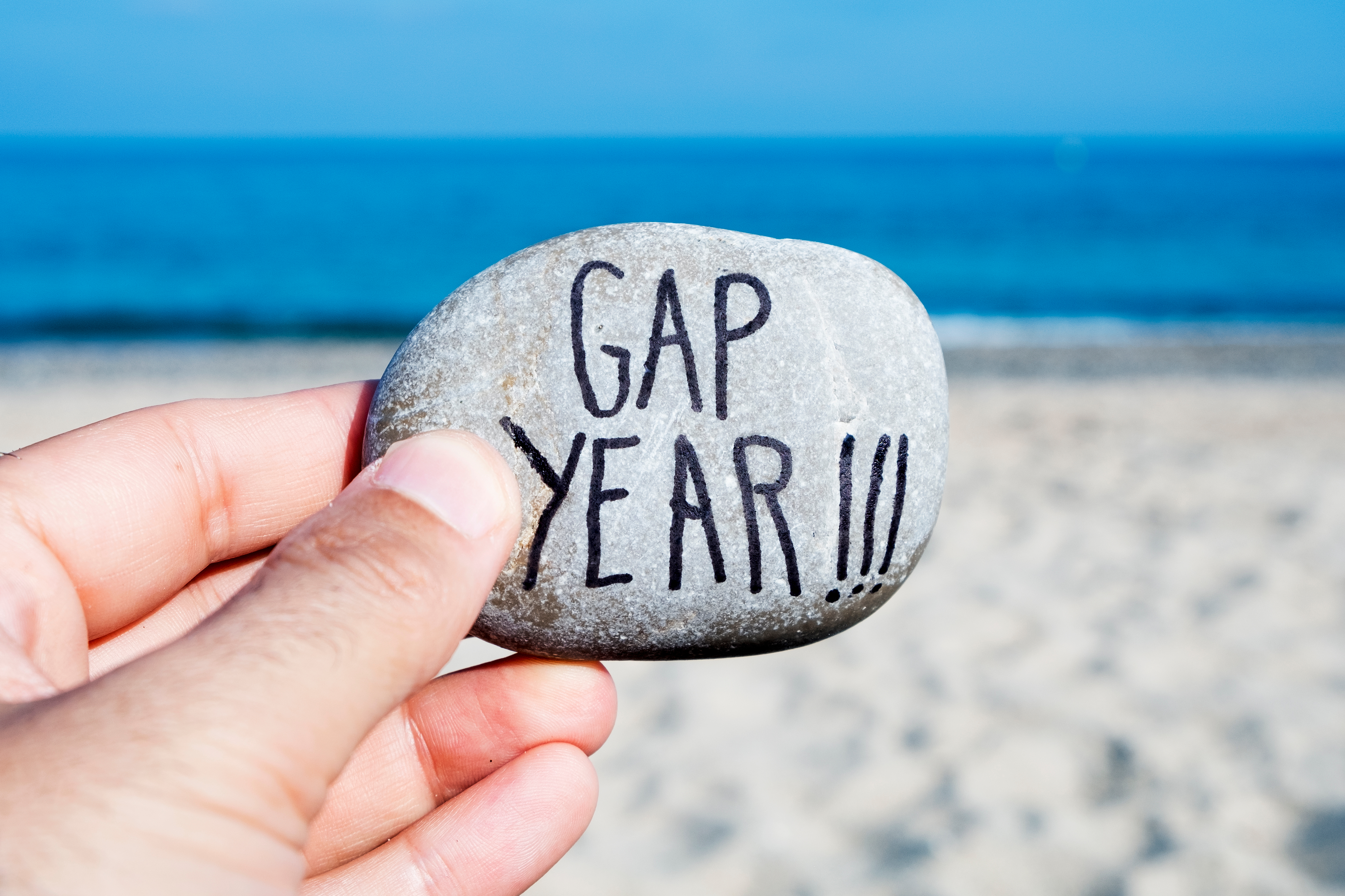 Gap Year feliratú kavicsot tart valaki a tengerpart homokja fölött