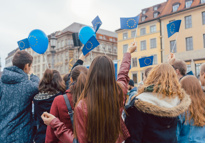 Fiatalok csoportja Európai Uniós zászlót és lufit lenget egy kisváros terén