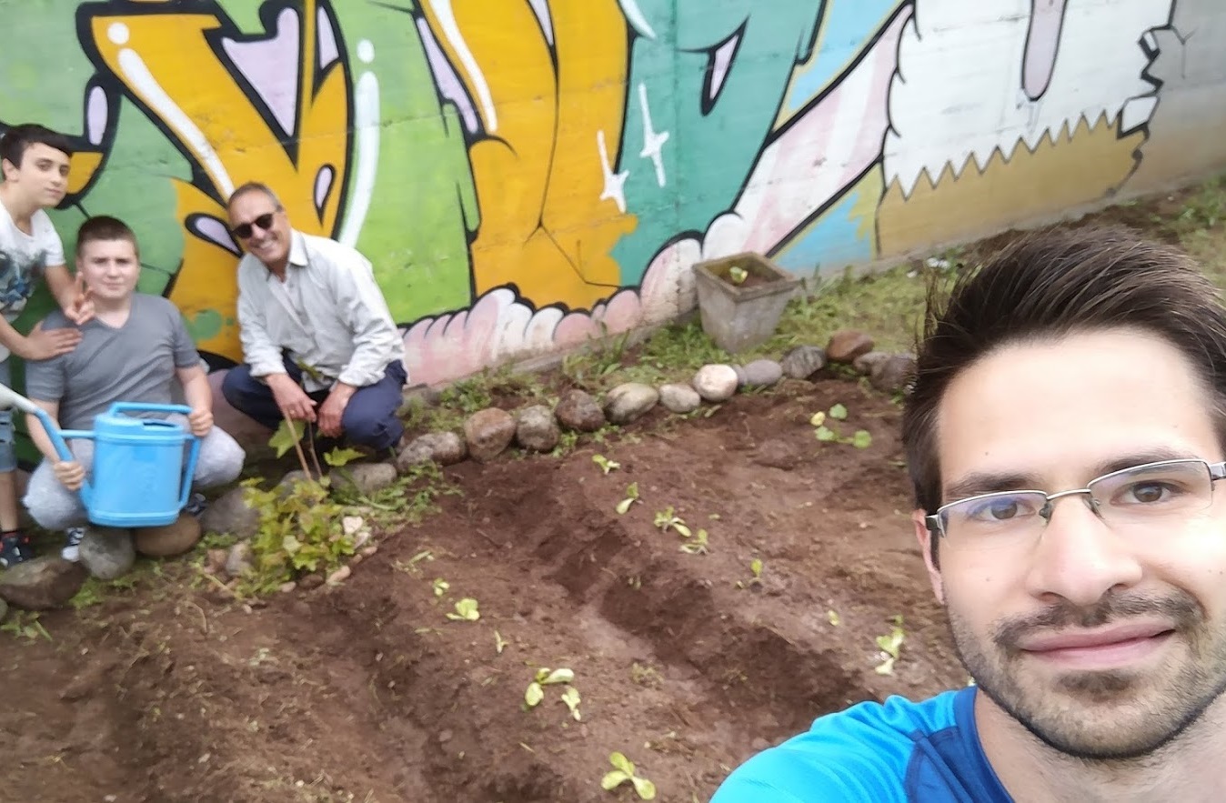 A QR52 ifjúsági központ grafitizett fala és virágágyása mellett szelfizik 3 kertészkedő ember Simon Gellérttel Milánóban